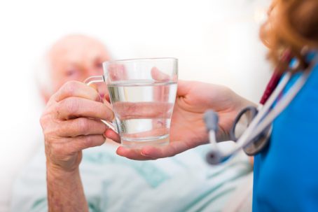 Elderly woman drinking water with the help of a nursing home caregiver.